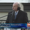 John Munchmeyer wearing coat, tie, earmuffs; standing outdoors at lectern with microphone, addressing gathering; TV screen capture; text marquee reads: 'Bill of Rights Anniversay' and 'Charlottesville' and station ID 'NBC 29'