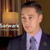 TV screen image with Reason logo and Nicholas Sarwark indoors wearing suit and tie on camera speaking, text reads 'Nick Sarwark Libertarian Party Chairman'