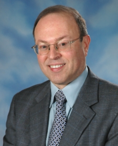 Murray Sabrin professional headshot, wearing grey suit, tie, blue shirt, glasses, smiling, 'blue sky' backdrop (color photo)