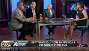 Image from TV screen of TV studio set with ‘K’ logo of show ‘Kennedy’ – seated on stools around table from left are Larry Sharpe, Matt Waters, Tim Silfies, and at right, hostess Lisa ‘Kennedy’ Montgomery – on screen is the text ‘Fox Business Network’ and ‘Kennedy’ and ‘Libertarian solutions to America’s health care problems’ (color image)