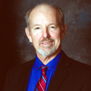 Jeff Hewitt headshot portrait wearing dark pinstripe blazer, royal blue shirt, red striped tie, goatee, looking at viewer, mottled grey-blue studio backdrop (color photo)