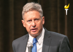 Gary Johnson wearing grey suit blue tie speaking at microphone before a national Libertarian Party audience in 2016 (color photo)